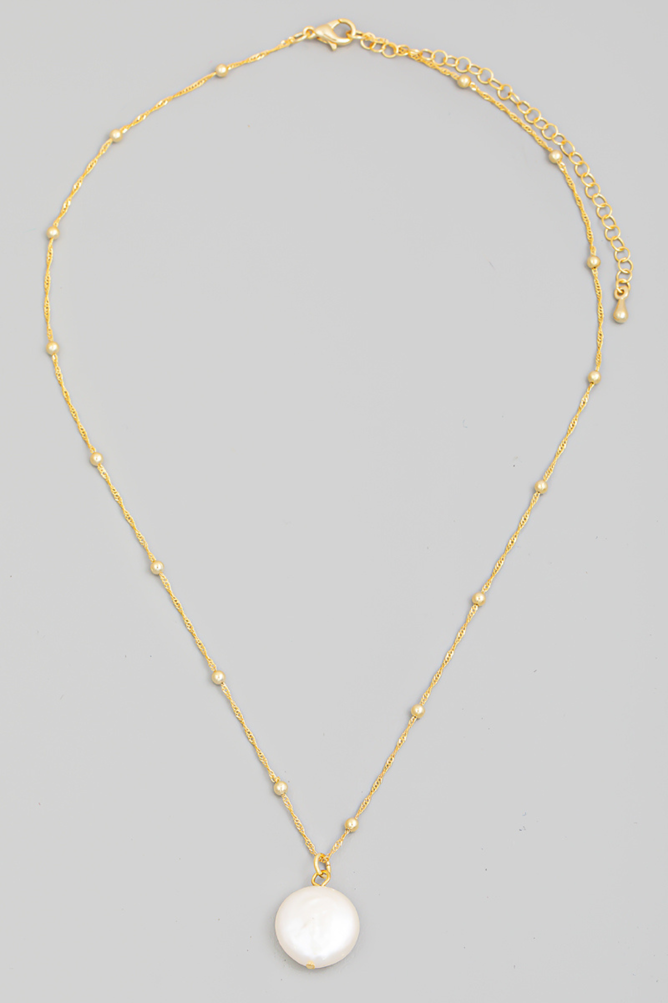 The image features the Woods Cove Pearl Charm Necklace by Larrea Cove, showcasing a delicate design with a pearl charm pendant. The necklace is elegantly displayed against a neutral background, highlighting its subtle shine and sophisticated appeal. It falls within the jewelry category, specifically under necklaces, and is associated with various tags indicating its new status and restock in 2024.