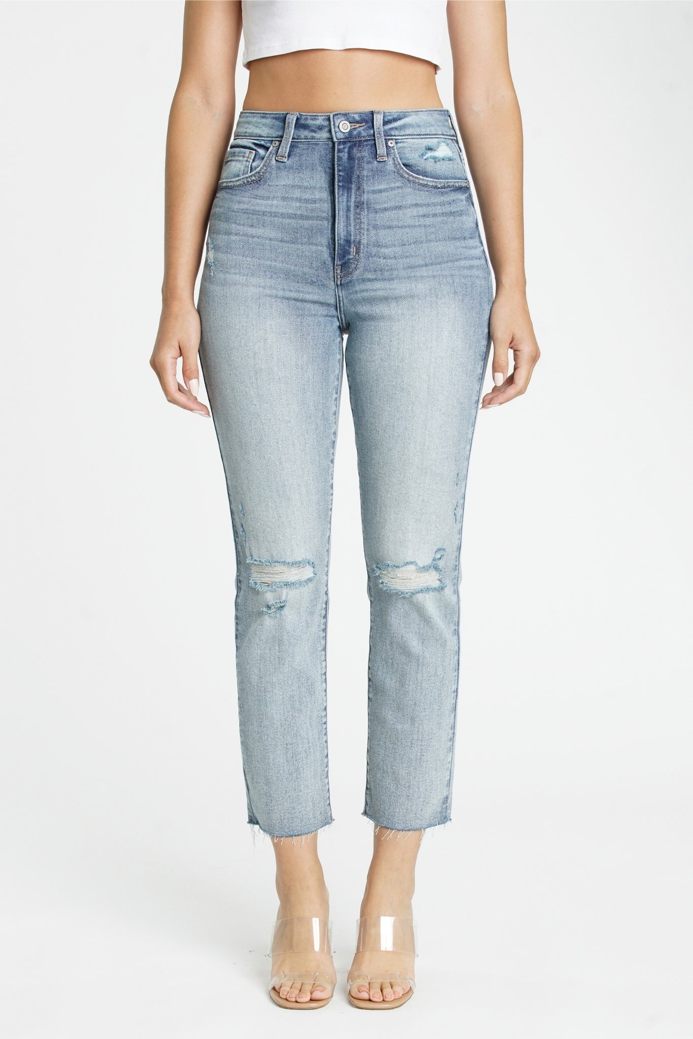 Alt text: A pair of Eunina Ally ultra high rise straight cropped jeans in a light wash denim color named Saguaro. The jeans feature whiskering and fading, a raw cut hem, distressed details at the knee, a five-pocket design, belt loops, and a hidden zip fly button closure. The model, who is 5'10" tall, is wearing the jeans styled with sunglasses.