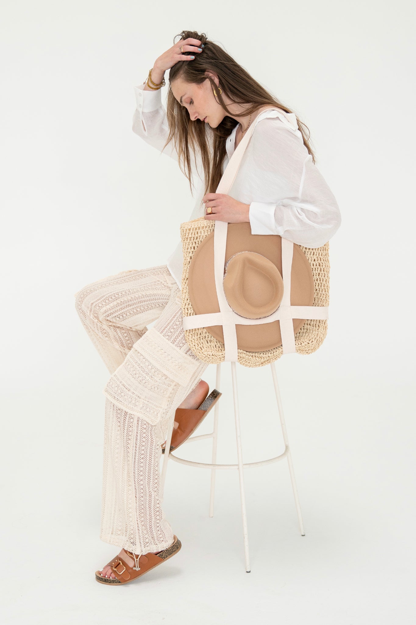 Beige straw Ironwood Bag by Larrea Cove, featuring built-in hat holder straps, ideal for beach vacations. The bag measures 16" L x 17" H x 1" W and is styled for summer wear.