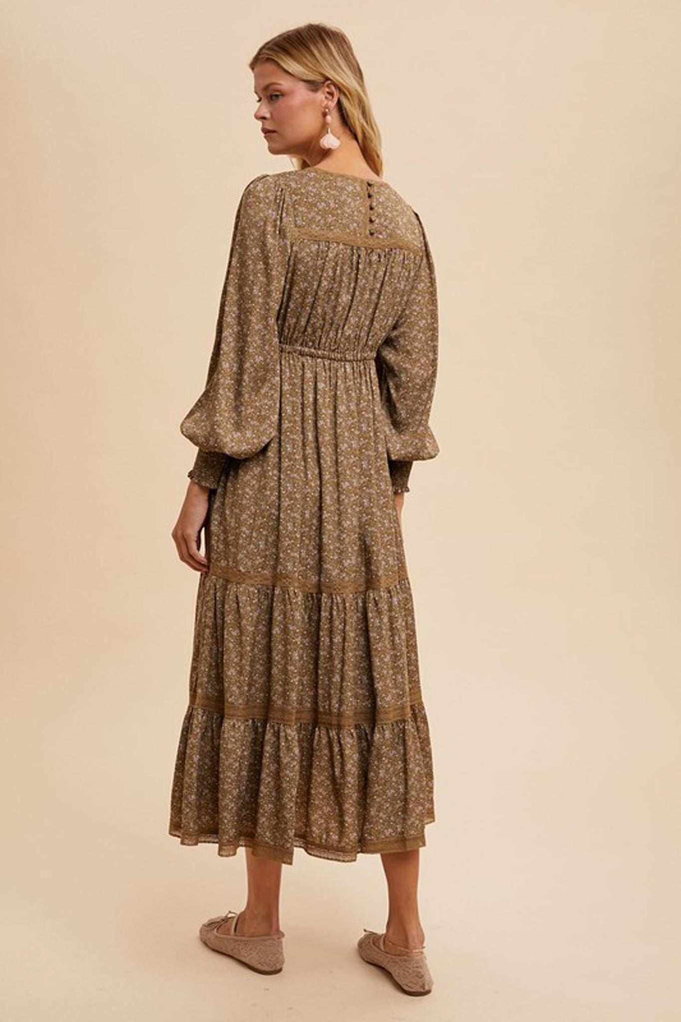 A floral maxi dress featuring lace trim, designed by Larrea Cove. The dress has a flowing silhouette and vibrant floral patterns, perfect for fall. Styled with sunglasses, it embodies a chic, seasonal look.