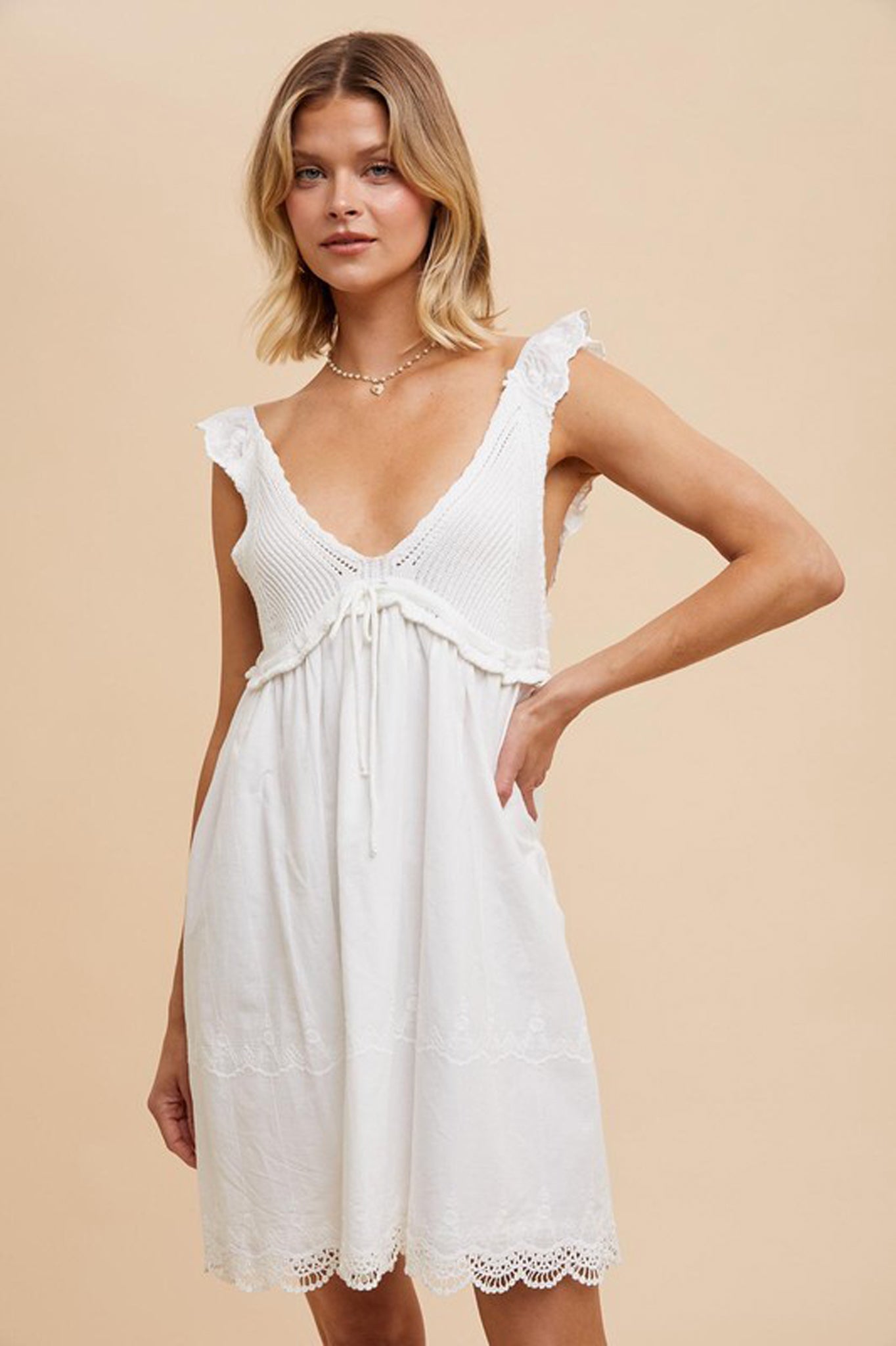 Alt text: A model wearing a V-Neck Crochet Mini Dress by Larrea Cove, showcasing a delicate crochet design. The dress features a flattering V-neckline and is made of 97% cotton and 3% polyester. The model, who is 5'10" with a bust of 32", waist of 24", and hips of 34", is styled with sunglasses, presenting a chic summer look.