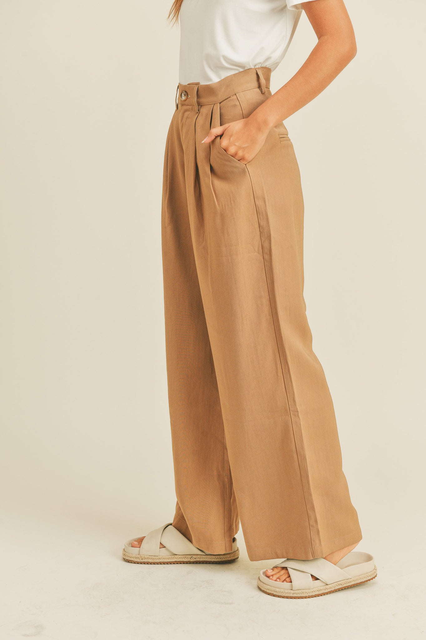 Arid Trousers in Camel by Larrea Cove, displayed on a neutral background. The trousers feature a relaxed fit and a warm camel color, suitable for casual wear. Accompanied by stylish sunglasses, emphasizing a fashionable look. Tags include bucket-30, MIOU MUSE, and new product from 2022, indicating a current sale.