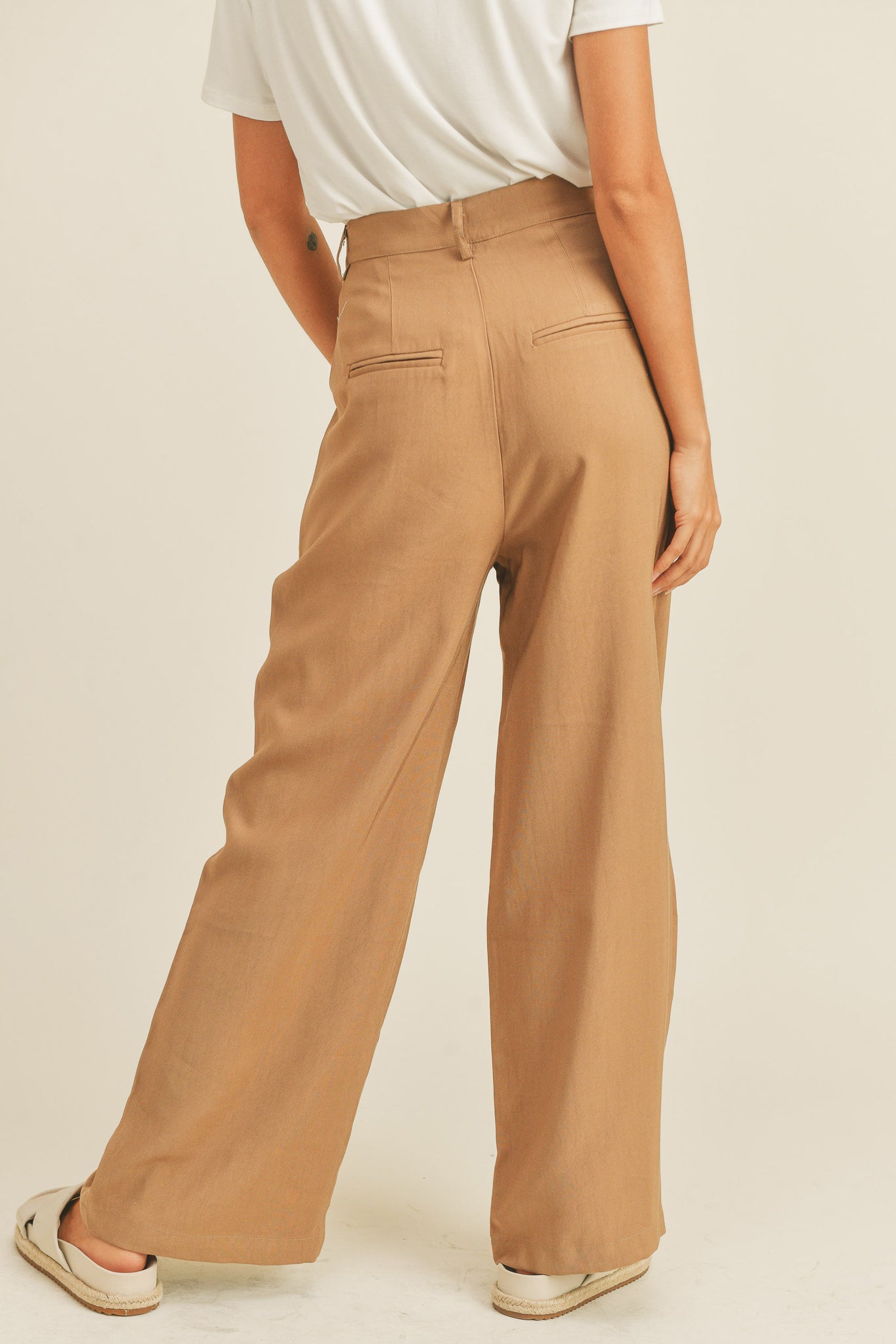 Arid Trousers in Camel by Larrea Cove, showcasing a stylish pair of camel-colored pants designed for comfort and versatility. The trousers are featured alongside sunglasses, emphasizing a fashionable look. Ideal for casual or semi-formal wear, these pants are part of the new collection launched in October 2022.