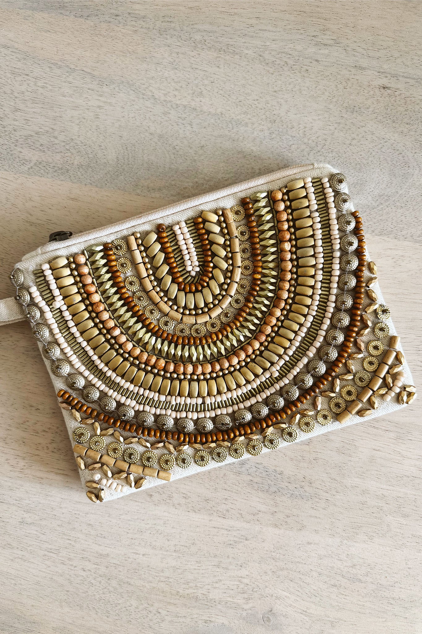 Allegra Beaded Wristlet in Gold by ANTIK KRAFT, featuring a stylish design with intricate beading and a wrist strap. The image showcases the wristlet's shimmering gold color, ideal for summer outings. A pair of sunglasses is also visible, adding a chic accessory touch.