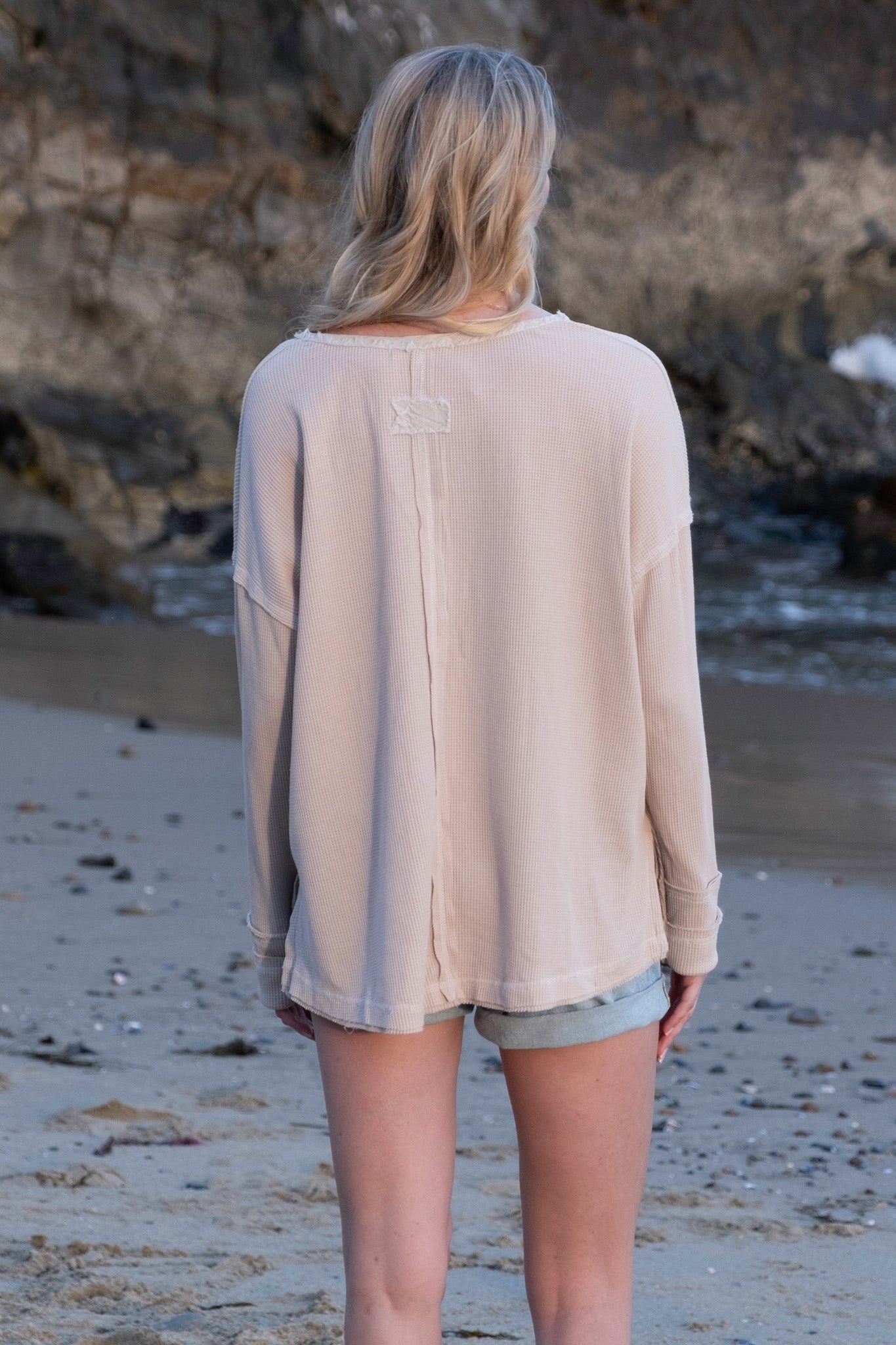 A garment washed thermal henley by Larrea Cove in a Poppi Seed color. The top features a classic henley design with buttons at the neckline, long sleeves, and a comfortable, relaxed fit. The fabric has a textured, thermal quality. The image suggests it is part of a new product line for November 2023 and is currently on sale.