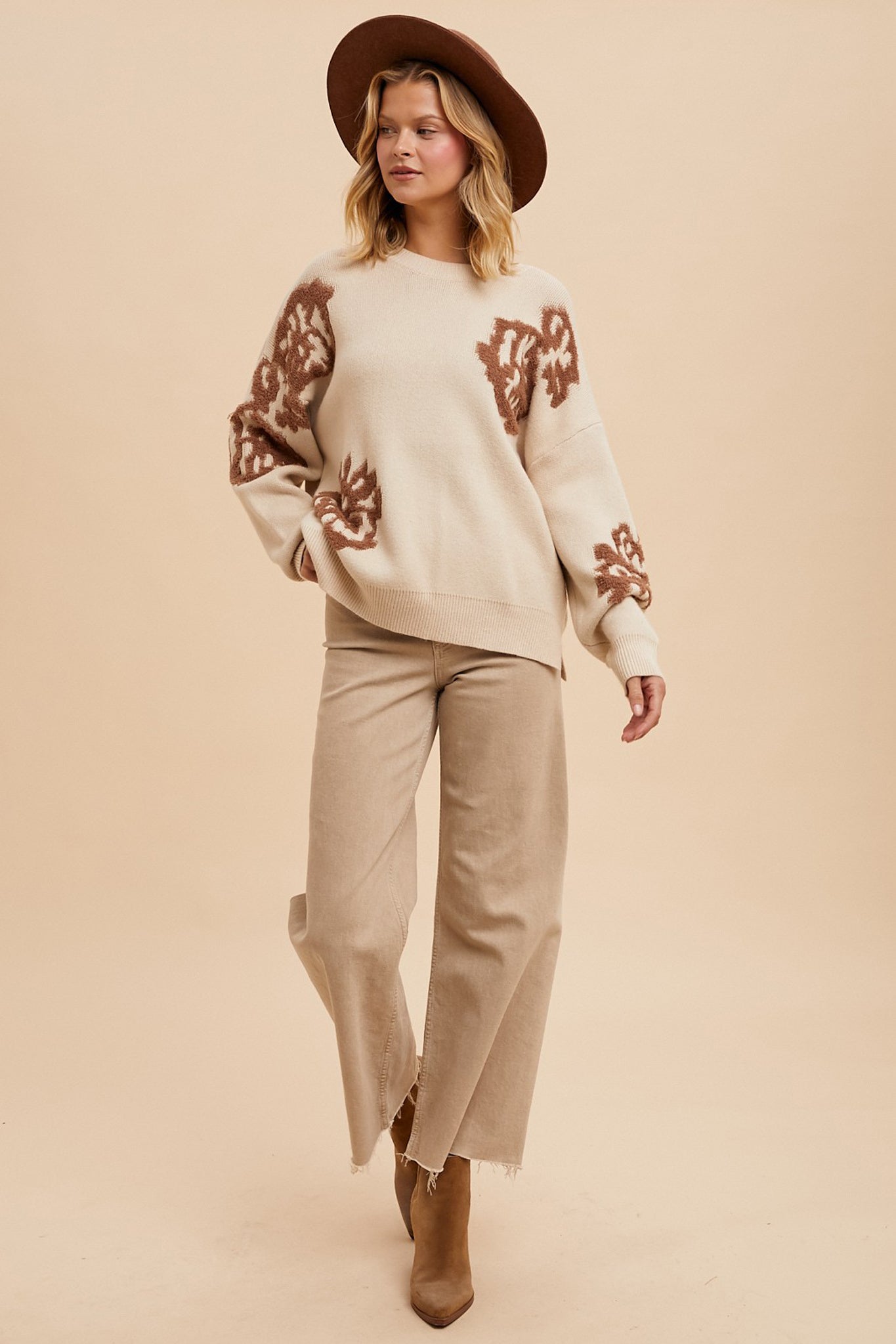 The image features a Lanta Floral Intarsia Knit Sweater by Larrea Cove, showcasing a vibrant floral design integrated into the knit pattern. The sweater is likely made from a soft, comfortable material, suitable for fall wear in 2024. It is displayed alongside stylish sunglasses, suggesting a fashionable look. The overall aesthetic is modern and appealing for autumn fashion.