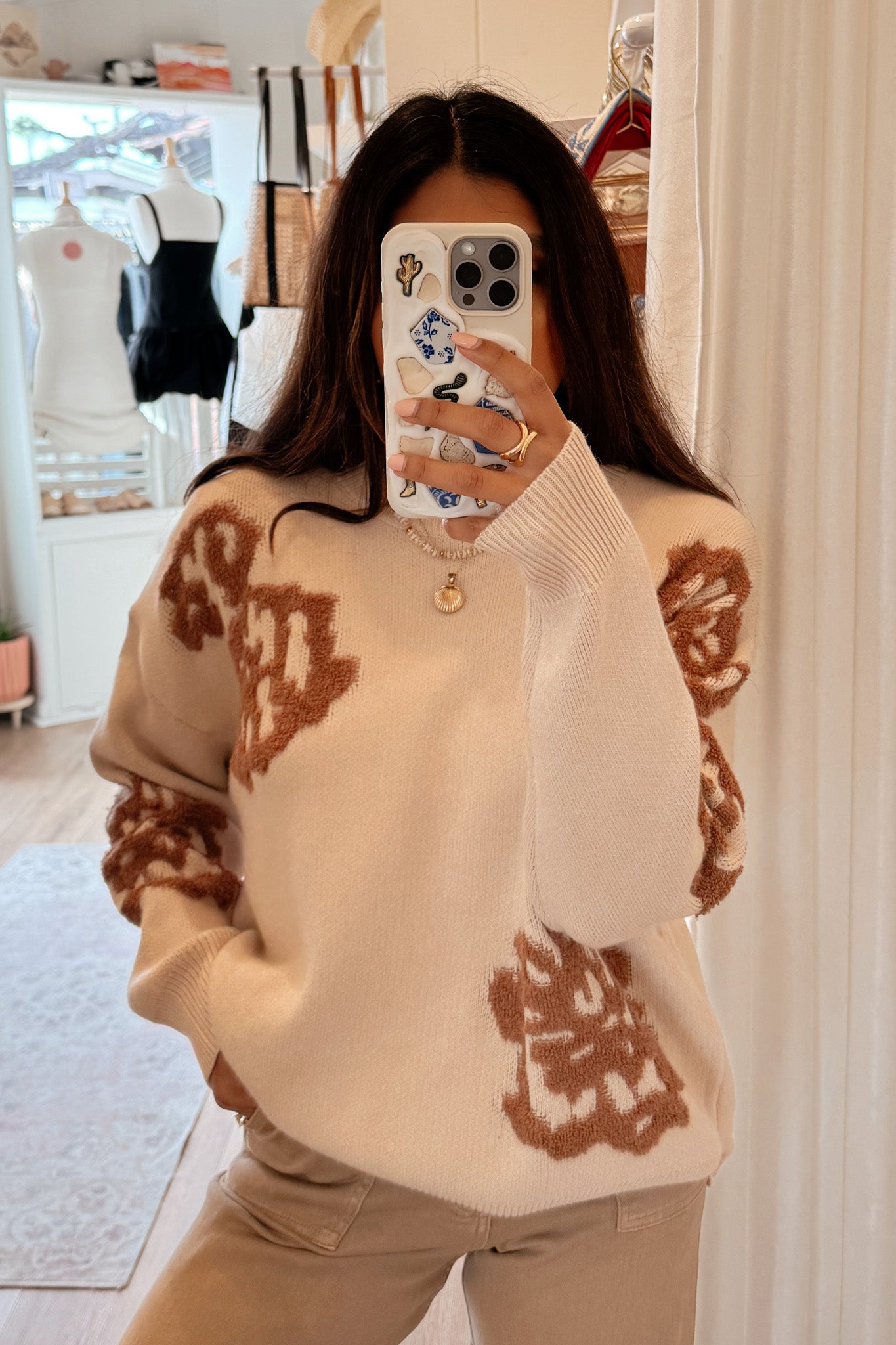 A model wearing the Lanta Floral Intarsia Knit Sweater by Larrea Cove, showcasing a relaxed fit and delicate floral design in neutral tones. The sweater is styled with jeans and sunglasses, set against a soft background. The model's height is 5'10" and she is wearing a size Small.