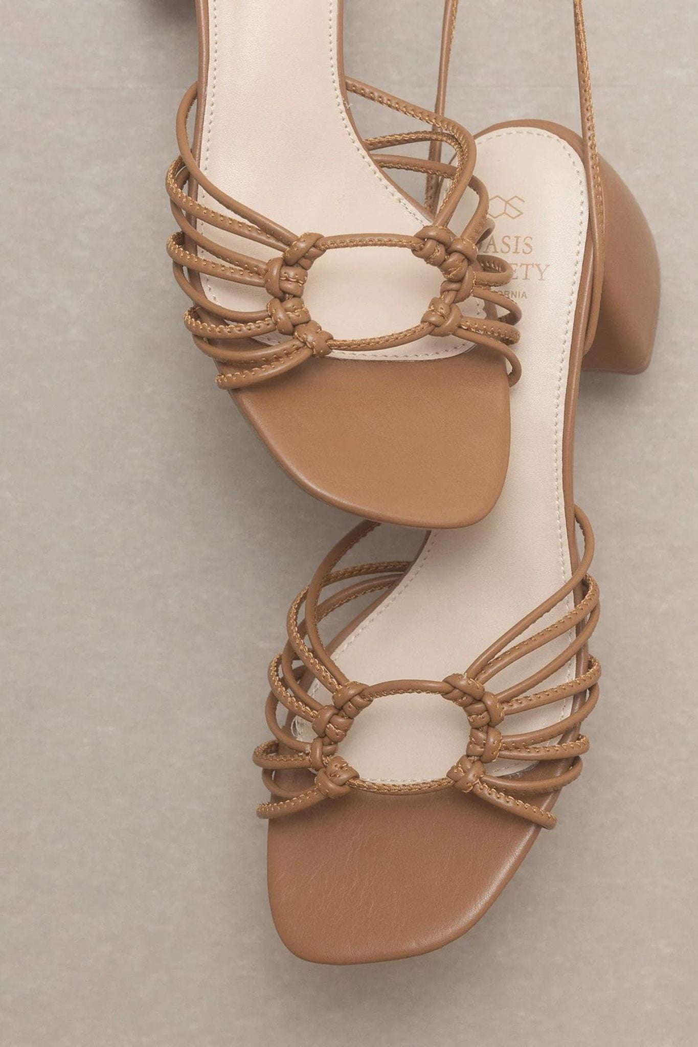 The Celia Brown Knotted Lace Up Heel by Oasis Society, featuring a stylish design with knotted details and a lace-up front, perfect for summer 2024. Accompanied by fashionable sunglasses.